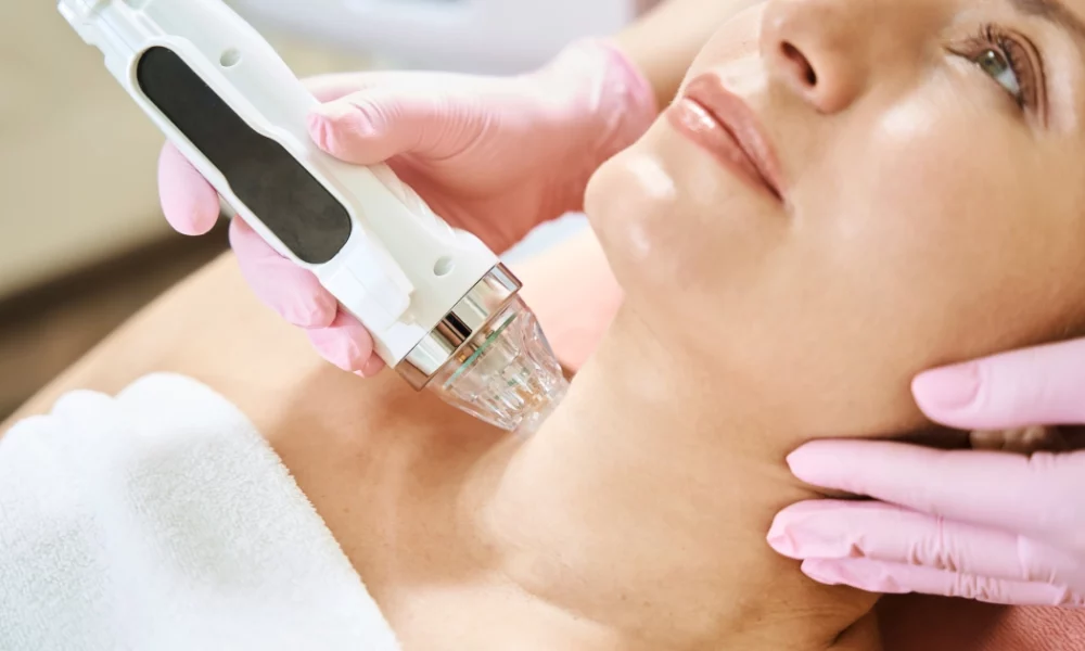 Woman receiving Microneedling in Riverside, CA on her neck, guided by a technician in pink gloves, in a bright clinic.